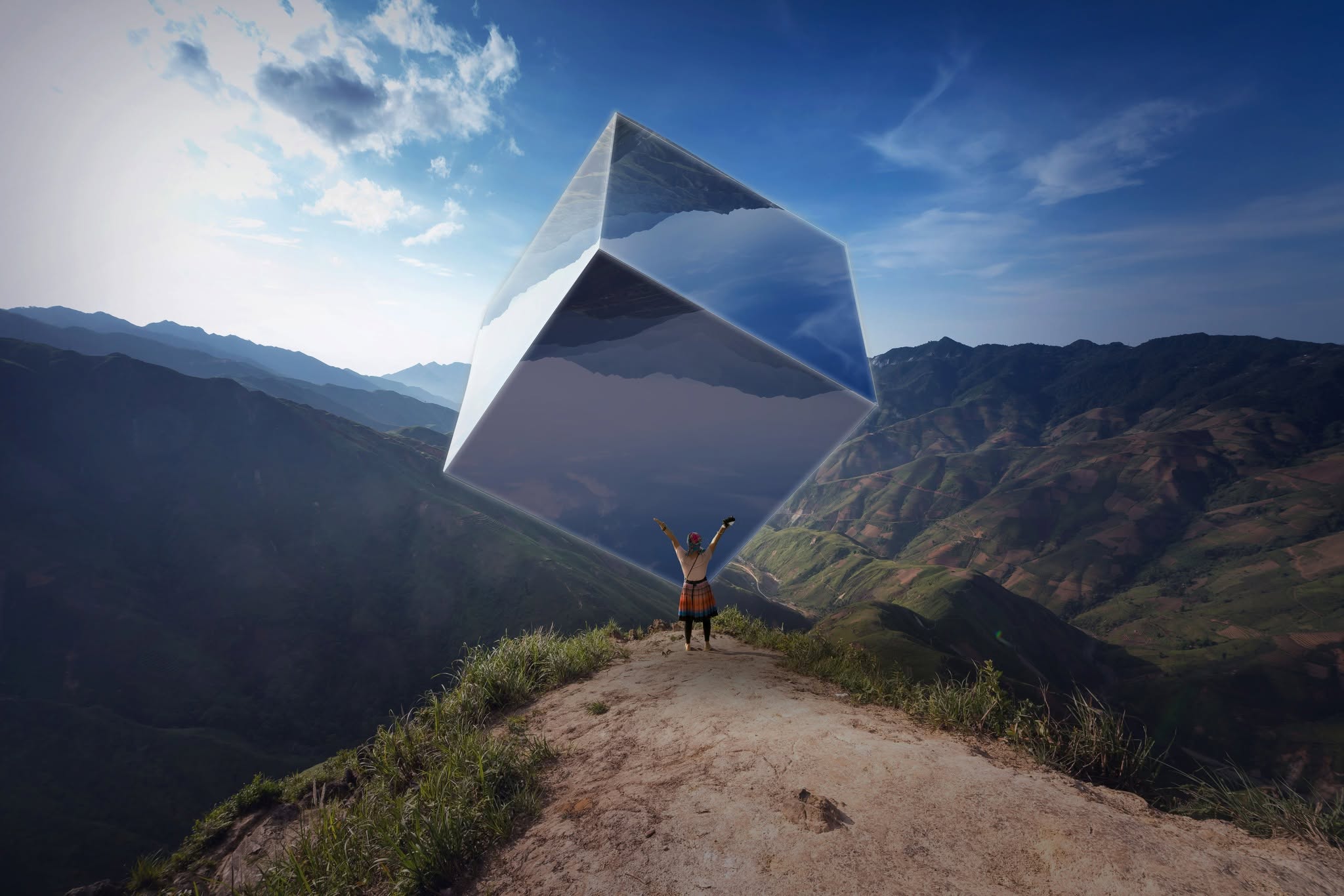 Photo composite: a person on a mountain ridge beneath a giant floating mirrored cube